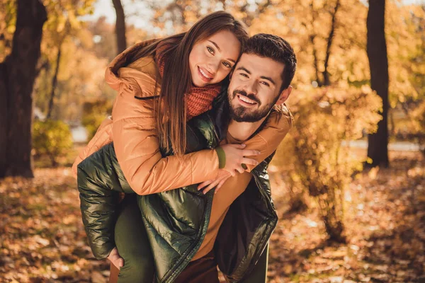 Photo of affectionate couple guy hug his girlfriend piggyback in autumn city outside forest park wear coats jackets — Stock Photo, Image