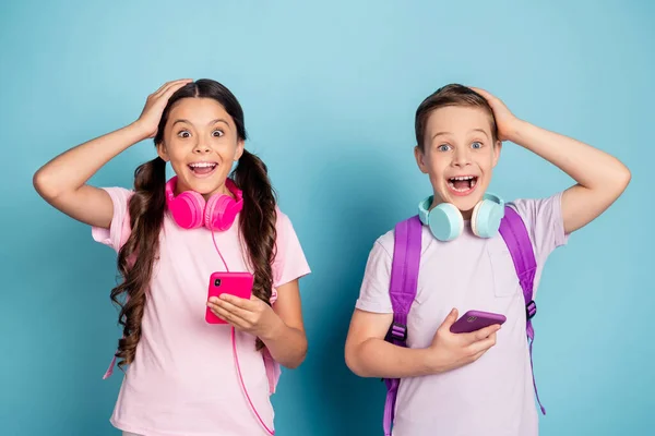 Foto de dos buenos amigos positivos sorprendidos usando auriculares usando teléfonos aislados sobre fondo de color azul —  Fotos de Stock