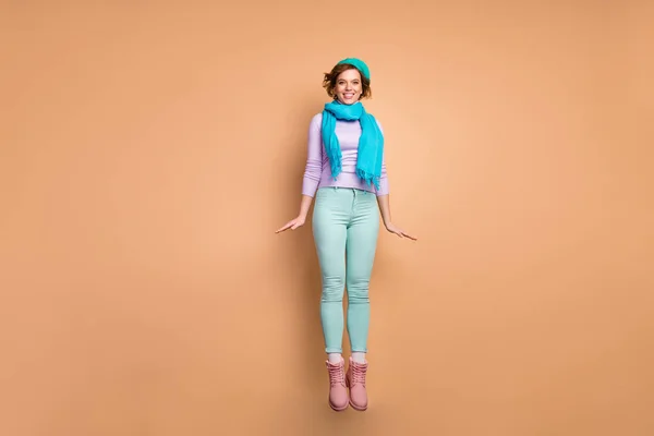 Πλήρης φωτογραφία του σώματος του αστεία όμορφη κυρία άλμα ψηλά καλή διάθεση χαρά φορούν μοβ πουλόβερ πράσινο παντελόνι ροζ μπότες μπλε μπερέ κασκόλ απομονωμένο μπεζ χρώμα φόντο — Φωτογραφία Αρχείου