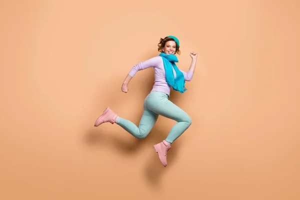 Πλήρης φωτογραφία προφίλ του σώματος του αστεία κυρία άλμα ψηλά σπεύδουν πώληση έκπτωση σεζόν άνοιγμα φορούν μωβ πουλόβερ πράσινο παντελόνι μπότες μπλε μπερέ κασκόλ απομονωμένο μπεζ χρώμα φόντο — Φωτογραφία Αρχείου