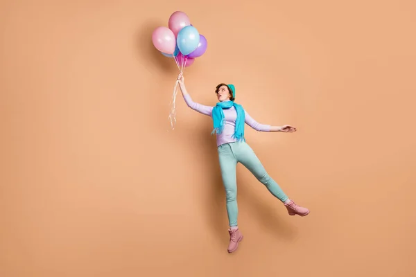 충격을 받은 여성이 높이뛰기를 하는 장면은 공중에 떠 있는 풍선을 많이 들고 있다. 바람이 부는 곳에는 보라색 점퍼그린 바지를 입고 있다. — 스톡 사진