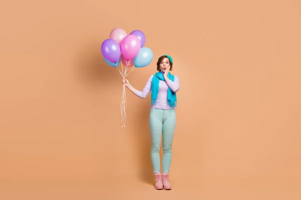 Foto de longitud completa de la señora bastante sorprendido llevar muchos globos de aire inesperada fiesta sorpresa desgaste lila jersey pantalones verdes botas boina bufanda aislado color beige fondo —  Fotos de Stock