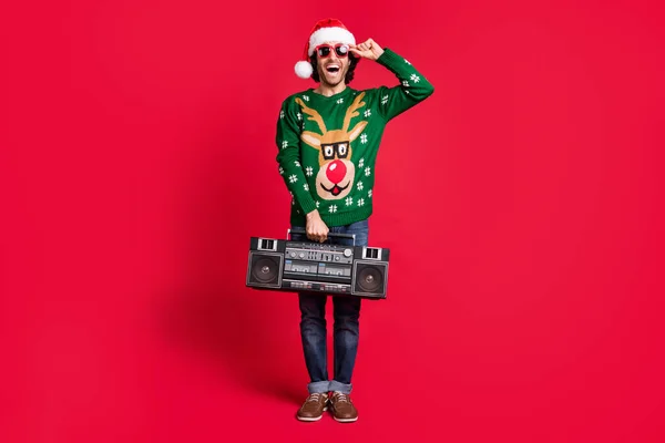 Full length body size view of attractive cheerful guy wearing Santa hat carrying cassette tape vintage boombox having fun enjoying leisure isolated bright vivid shine vibrant red color background — Zdjęcie stockowe