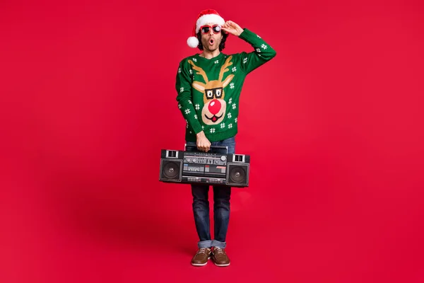 Full length body size view of attractive funny amazed childish guy wearing Santa hat carrying boombox having fun pout lips leisure isolated bright vivid shine vibrant red color background — Zdjęcie stockowe