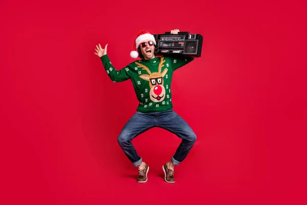 Ganzkörpergröße Ansicht der attraktiven froh fröhlich kindischen Kerl trägt Weihnachtsmannmütze tragen Boombox Spaß beim Tanzen Narren Freizeit isoliert hell lebendigen Glanz lebendige rote Farbe Hintergrund — Stockfoto