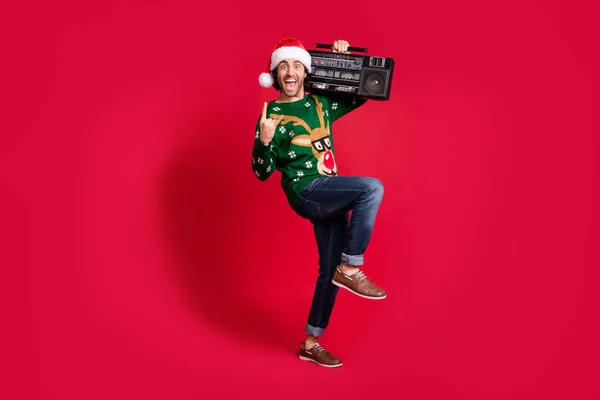 In voller Länge Körpergröße Ansicht seiner er attraktiv froh fröhlich fröhlich Kerl trägt Weihnachtsmütze tanzen tragen Boombox Spaß Show Horn Zeichen isoliert hell lebendigen Glanz lebendige rote Farbe Hintergrund — Stockfoto