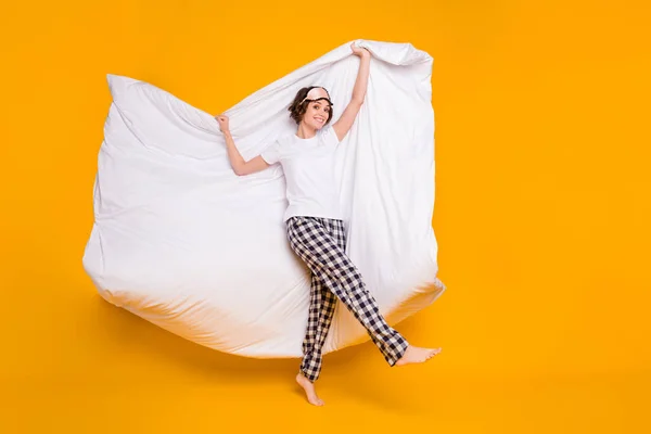 Foto de comprimento total de senhora alegre segurar cobertor quente acima da cabeça acordar humor brincalhão dança desgaste energético máscara branco t-shirt xadrez pijama calças descalço isolado cor amarela fundo — Fotografia de Stock