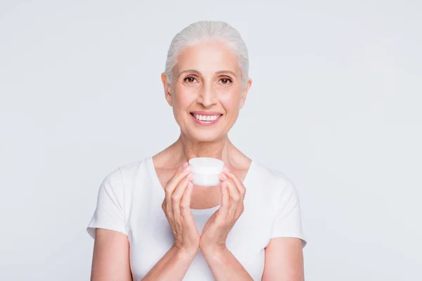 Retrato da linda avó segurando frasco com procedimento nutritivo olhando para a câmera vestindo elegante camiseta na moda isolada sobre fundo branco — Fotografia de Stock