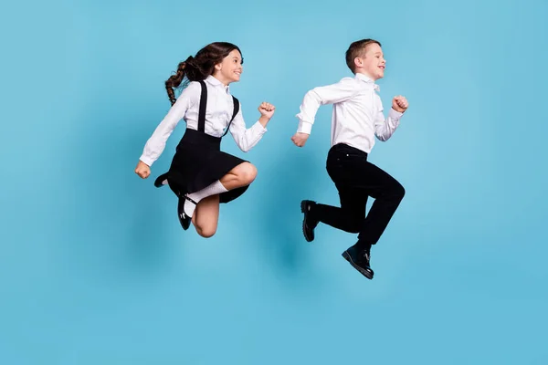 Volledige lengte profiel foto van twee kleine meisje jongen schoolkinderen broer zus klasgenoten springen gelukkig run school concept dragen wit shirt zwart broek jurk geïsoleerde blauw kleur achtergrond — Stockfoto