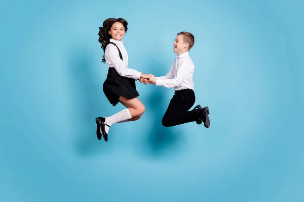 Foto de perfil de longitud completa de dos compañeros de clase opuestos niña niño colegiales saltar de la mano diversión después de la escuela usar camisa blanca pantalones negros vestido aislado color azul fondo — Foto de Stock