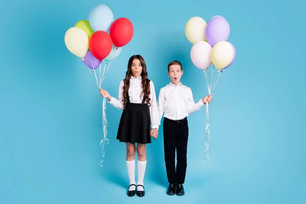 Ganzes Foto von zwei kleinen Mädchen Junge Schüler besten Freunde halten Hände Luftballons erstaunt beobachten Klassenkameraden tragen weißes Hemd schwarze Hose Kleid Schuhe isoliert blaue Farbe Hintergrund — Stockfoto