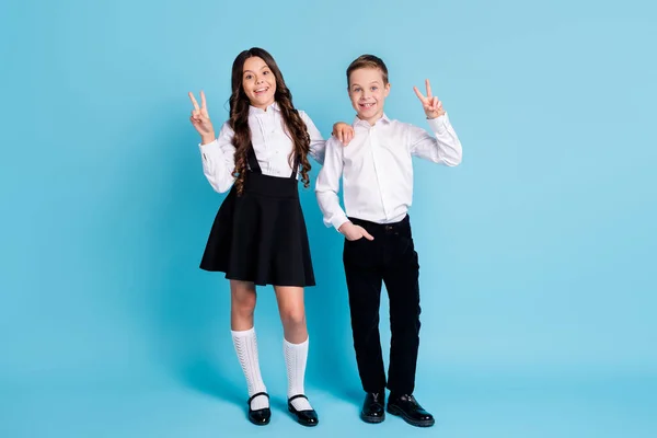 Salut camarades de classe. pleine longueur photo de deux fille modèle garçon écoliers meilleurs amis soeur frère montrer v-signe porter uniforme blanc chemise noir pantalon robe chaussures isolé bleu couleur fond — Photo