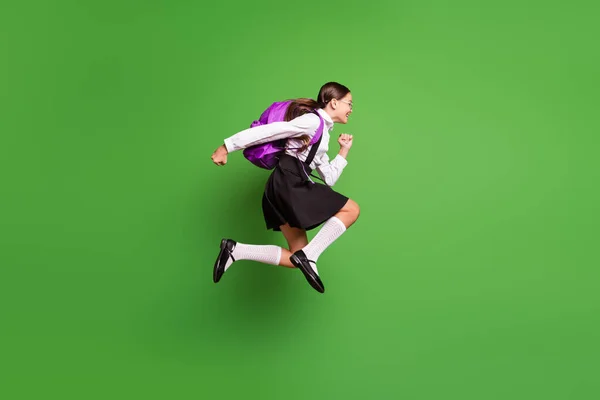 Foto portrét brunetky dívka s copánky běží do školy skákání s růžovým batohem izolované na živém zeleném pozadí — Stock fotografie