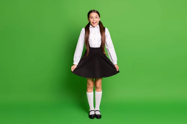 Retrato fotográfico de una chica conmocionada mostrando su uniforme escolar aislado sobre un fondo de color verde vivo — Foto de Stock
