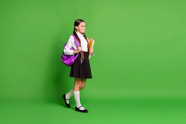 Foto retrato de menina andando segurando livros na mão vestindo costas rosa no ombro isolado no fundo de cor verde vívido com copyspace — Fotografia de Stock