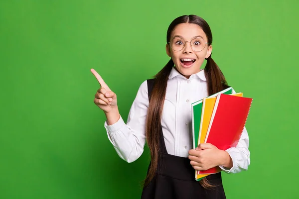 Foto retrato de estudante animado apontando dedo para copyspace segurando cadernos isolados em fundo de cor verde vívido — Fotografia de Stock