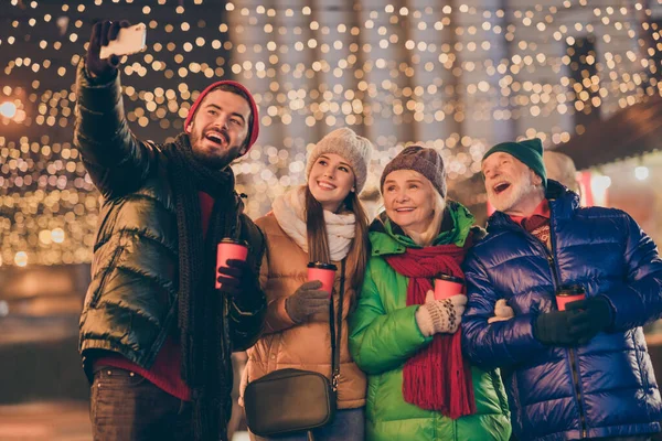 Фото большой семьи четыре члена x-mas сбор держать кружку сделать селфи телефон видеокассета носить верхнюю одежду шляпу шарф пальто поколения ночной улице парк магическое освещение на открытом воздухе — стоковое фото