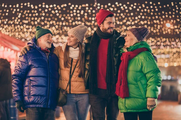 Foto de família cheia quatro membros reunião abraçar passar fim de semana noel juntos depois de muito tempo de separação milagre do ano novo comprar lembranças multi-geração noite iluminação de rua feira ao ar livre — Fotografia de Stock