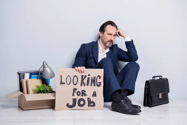 Full length photo of loser worker mature aged guy jobless man hold placard need work sit floor briefcase belongings box stuff lost everything wear suit shoes isolated grey background — Stock fotografie