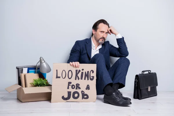 Full length photo of loser worker mature aged guy jobless man hold placard need work sit floor passessment αντικείμενα κουτί πράγματα έχασε τα πάντα φορούν κοστούμι παπούτσια απομονωμένο γκρι φόντο — Φωτογραφία Αρχείου