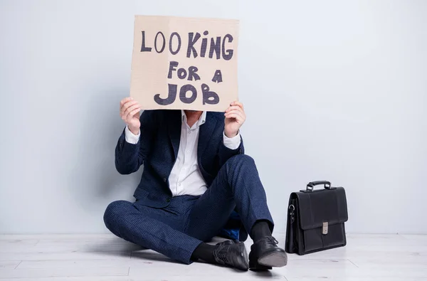 Full size photo of loser fired worker mature guy business man jobless man hold carton placard hide face need work sit floor briefcase search office wear suit shoes isolated grey background — Fotografia de Stock