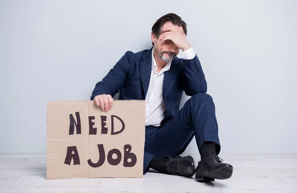 Full length photo of unforgrated worker mature guy lost work jobless man hold carton placard seek work sit floor hide eyes look wear blue suit shoes απομονωμένο γκρι φόντο — Φωτογραφία Αρχείου