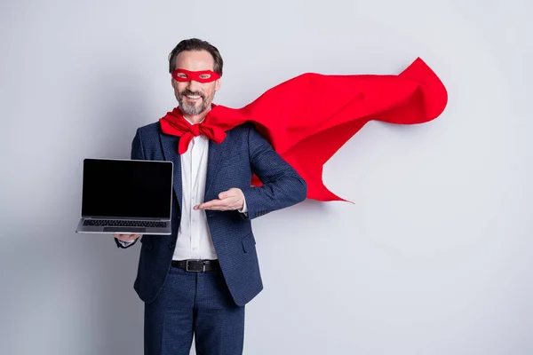 Foto de alegre idade maduro negócio cara super-herói traje segurar laptop mostrando novo dispositivo venda gerente moderno usuário desgaste terno vermelho máscara capa voando isolado fundo cinza — Fotografia de Stock