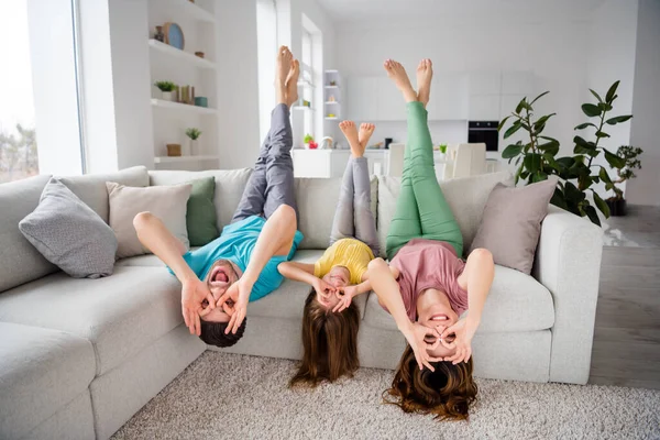 Volledige lichaam foto van positieve dwaas drie mensen mama papa klein meisje kind hebben rust ontspannen zitten gezellige bank ondersteboven maken ok teken bril vingers kijken grappig in huis binnen — Stockfoto