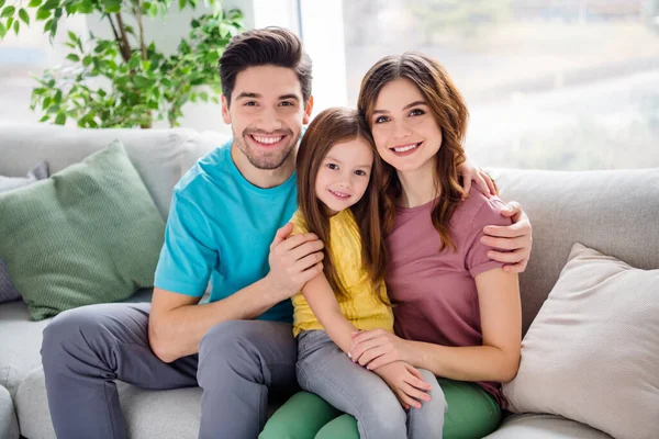 Foto de positivo tres personas amorosas madre padre abrazo abrazo abrazo niña pequeña niño sentarse sofá en casa en el interior — Foto de Stock