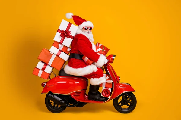 Profil Seitenansicht seiner er schön lustig fröhlich weißhaarige Nikolaus Reiten Moped beeilen sich Eile Lieferung bringen Stapel Geschenkboxen isoliert hell lebendigen Glanz lebendige gelbe Farbe Hintergrund — Stockfoto