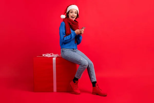 Longitud completa vista del tamaño del cuerpo de ella ella agradable atractiva chica alegre sorprendido sentado en gran regalo grande usando aplicación gadget 5g tienda servicio orden aislado brillante brillo vivo vibrante color rojo fondo — Foto de Stock