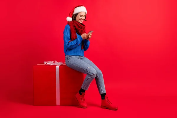 Full length body size άποψη της αυτή ωραία ελκυστική αρκετά εστιασμένη χαρούμενο κορίτσι κάθεται σε μεγάλο μεγάλο δώρο χρησιμοποιώντας συσκευή gadget app 5g απομονωμένο φωτεινό έντονο λαμπερό κόκκινο χρώμα φόντο — Φωτογραφία Αρχείου