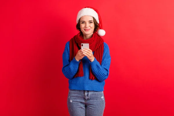 Photo positive girl in santa claus cap use smartphone enjoy christmas season shopping tradition sales discount wear denim jeans blue knitted sweater isolated bright shine color background — Stock Photo, Image