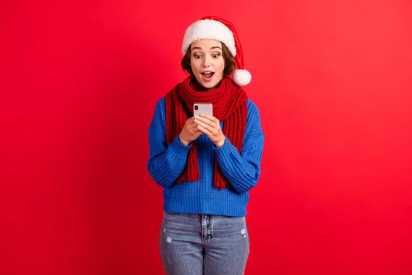 Schockiert erstaunt Mädchen in Santa Claus Mütze verwenden Smartphone erhalten Weihnachtsgratulation berühmten Social-Media-Blogger tragen blauen Strickpullover Jeans isoliert hellen Glanz Farbe Hintergrund — Stockfoto