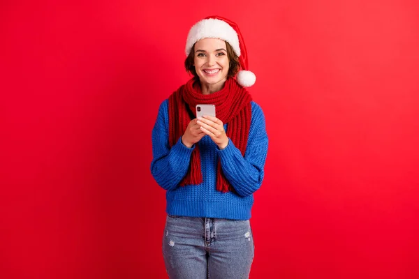 Foto positive Mädchen in Santa Claus Kopfbedeckung Mütze verwenden Smartphone genießen Weihnachten Neujahr Kommunikation Chat tragen blau gestrickte Pullover Jeans isoliert hellen Glanz Farbe Hintergrund — Stockfoto