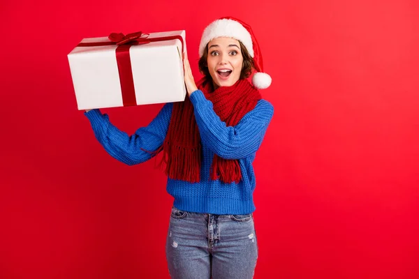 Fénykép a meglepett lány Santa Claus fejfedő kap karácsonyi vidám advent ajándék doboz lenyűgözött shake kopás kék kötött pulóver farmer farmer elszigetelt felett fényes fény háttér — Stock Fotó