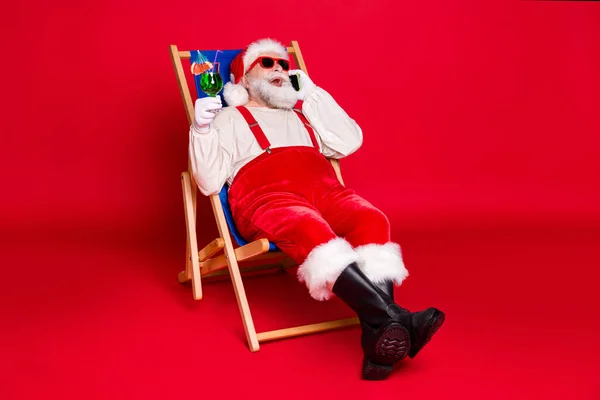 Retrato dele ele bonito alegre barbudo gordura Santa hipster sentado na cadeira beber mojito chamando no exterior amigo itinerante serviço celular isolado brilhante brilhante brilho vibrante cor vermelha fundo — Fotografia de Stock