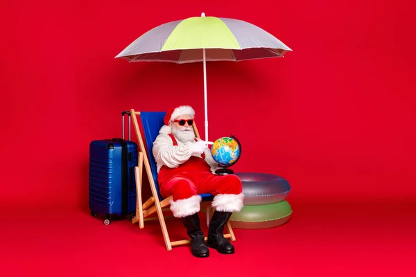 Retrato dele ele bonito bonito barbudo gordura Papai Noel turista sentado na cadeira segurando em mãos globo escolhendo viagem destino isolado brilhante brilhante brilho vibrante cor vermelha fundo — Fotografia de Stock