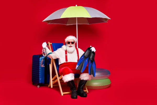 Portrait of his he nice handsome cheerful bearded fat Santa sitting in chair preparing voyage holding in hands swim equipment leisure resort isolated bright vivid shine vibrant red color background — Stock Photo, Image