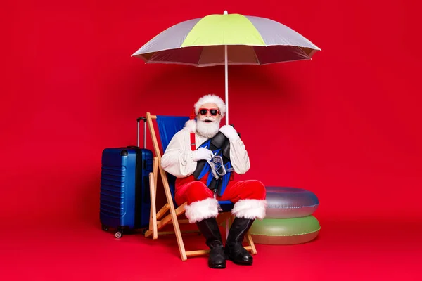 Retrato de su buen guapo alegre barbudo gordo Santa sentado en silla abrazando equipo de snorkel actividad hobby deporte submarino aislado brillante brillo vivo vibrante color rojo fondo — Foto de Stock