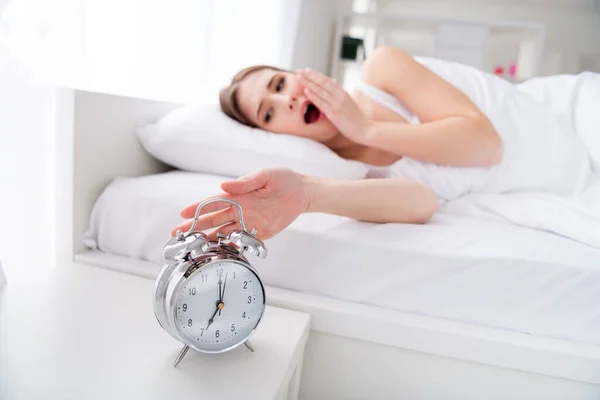 Foto de perfil de la encantadora joven acostada cama de dormir sábanas blancas manta ropa metal despertador reloj anillo siete oclock temprano por la mañana bostezar perezoso trabajador bostezar dormitorio en el interior — Foto de Stock