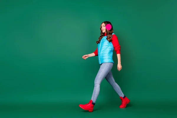 Foto de longitud completa de bastante encantador paseo joven ciudad parque camino a casa clima frío niebla desgaste rosa calentadores de oídos chaleco azul pantalones vaqueros suéter rojo botas aisladas de color verde fondo —  Fotos de Stock