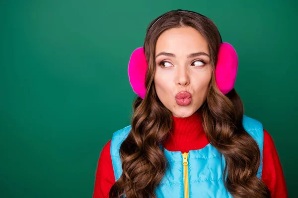 Closeup photo of lovely cute young lady truted lips send air kiss look empty space wait response feedback wear pink ear warmers blue zip vest red sweater isolated green color background — Stock fotografie