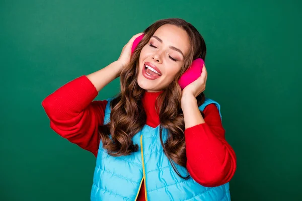 Foto av ganska söt ung dam drömmande öppen mun blunda låtsas lyssna musik surrande vaggvisa bära rosa öra värmare blå väst röd tröja isolerad grön färg bakgrund — Stockfoto