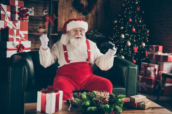 Addicted passionné barbe grise santa claus assis canapé profiter x-Noël noël événement jouer jeu vidéo gagner succès soulever poings porter casquette casque dans la maison à l'intérieur noel arbre à feuilles persistantes ornement — Photo