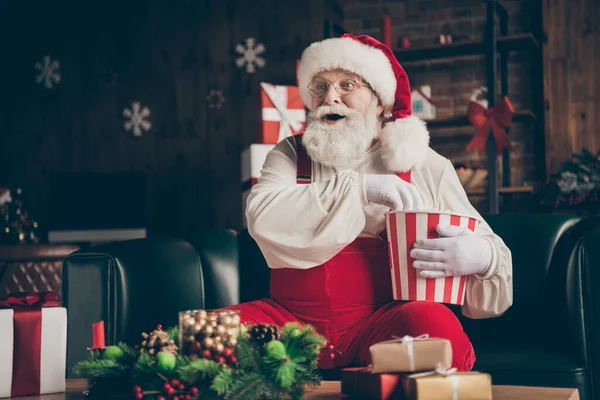 Foto de animada barba cinza santa claus sentar sofá assistir x-mas natal televisão comer pop corn box surpreendido advento desgaste chapéu vermelho headwear em casa dentro de casa noel ornamento — Fotografia de Stock