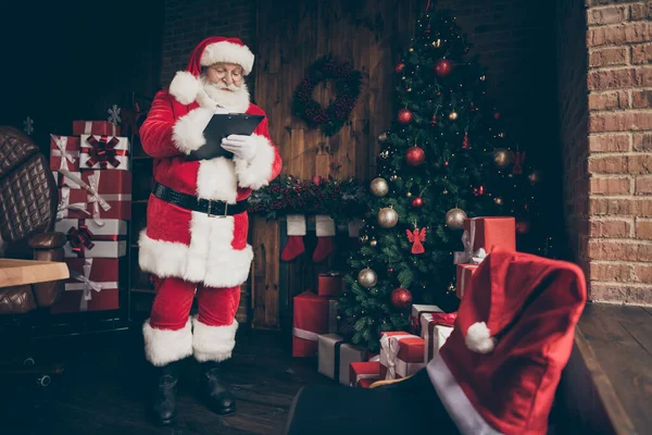 Pleine longueur photo blanc cheveux gris barbe Père Noël claus préparer x-Noël noël écrire presse-papiers organiser rêve cadeau livraison minuit porter casquette ceinture bottes maison à l'intérieur noel tinsles boules — Photo