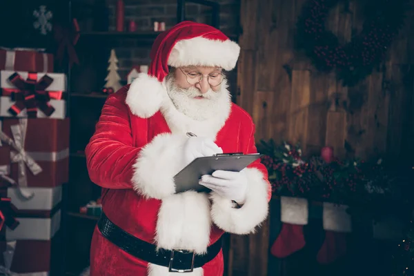 Photo fée joyeux houx barbe grise Père Noël claus préparer x-Noël fête événement écrire presse-papiers commander cadeau cadeau nuit minuit livraison porter casquette dans la maison à l'intérieur avec ornement noel — Photo