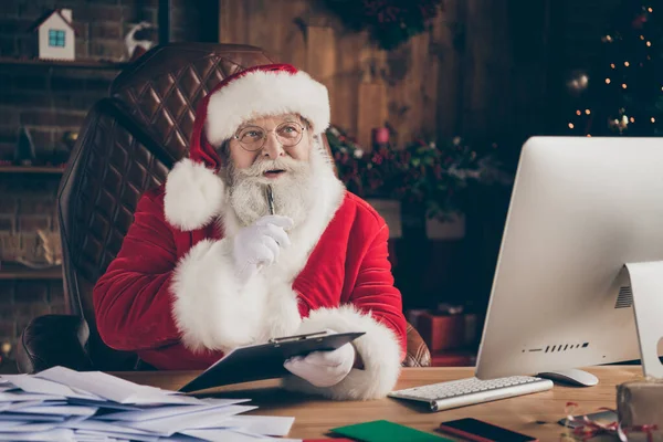 Whait se i. Pensamento pensativo Papai Noel claus sentar tabela preparar x-mas Natal ordem do presente escrever prancheta acho que os pensamentos têm ideias de ano novo louco usar boné em casa dentro de casa Natal árvore enfeites — Fotografia de Stock