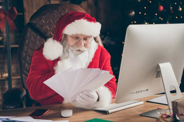 Foto von fokussierten Weihnachtsmann Weihnachtsarbeiter wollen Geschenk vorbereiten Geschenk Weihnachten Nacht Mitternacht lesen Wunschliste Briefe Umschlag berühren grauen Bart denken im Haus drinnen mit Dekoration — Stockfoto